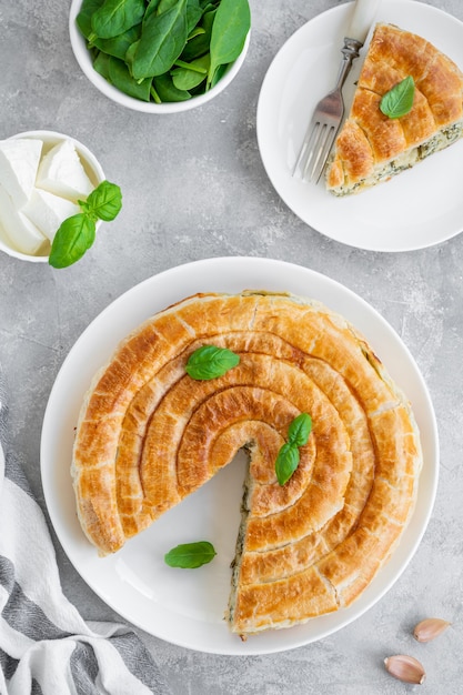 Griechischer Kuchen Spanakopita mit Feta-Käse und Spinat auf einem weißen Teller auf einem grauen Betonhintergrund