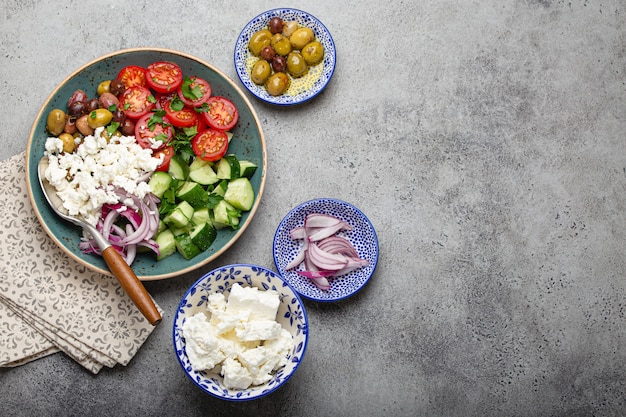 Griechischer mediterraner Salat mit Tomaten, Feta-Käse, Gurken, ganzen Oliven und roten Zwiebeln in blauer Keramikplatte auf grauem Betonhintergrund von oben, traditionelle Vorspeise Griechenlands mit Kopierraum