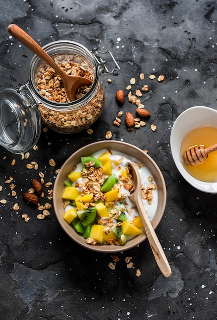 Griechischer Naturjoghurt mit tropischen Früchten und Müsli auf dunklem Hintergrund Draufsicht