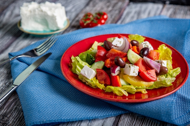 Griechischer Salat aus frischer Gurke, Tomate, Paprika, Salat, roten Zwiebeln, Feta-Käse und Oliven mit Olivenöl auf Holzfläche. Gesundes Essen