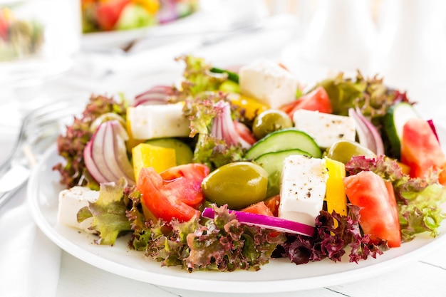 Griechischer Salat Frischer Gemüsesalat mit Tomaten, Zwiebeln, Gurken, Paprika, Oliven, Salat und Feta-Käse. Griechischer Salat auf einem Teller auf einem weißen Tisch