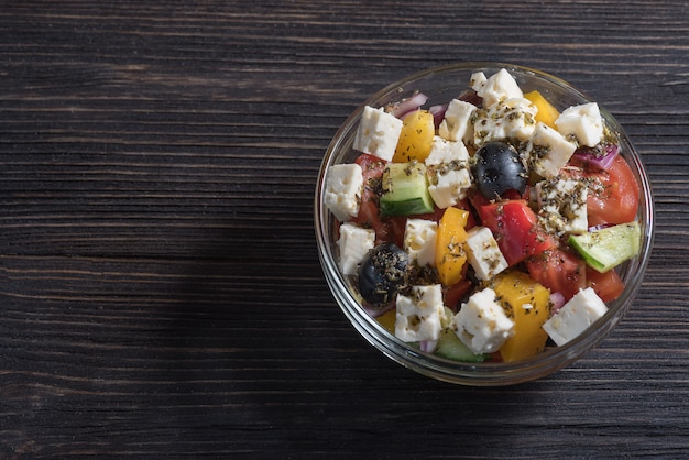 Griechischer Salat im Glasteller auf Holztischhintergrund.