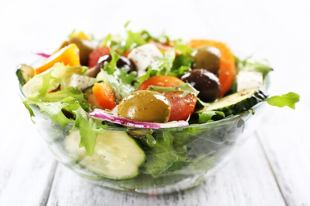 Griechischer Salat in Glasschale auf farbigem Holztischhintergrund