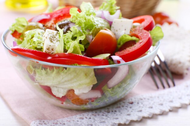 Griechischer Salat in Glasschale mit Gabel und Gemüsehintergrund