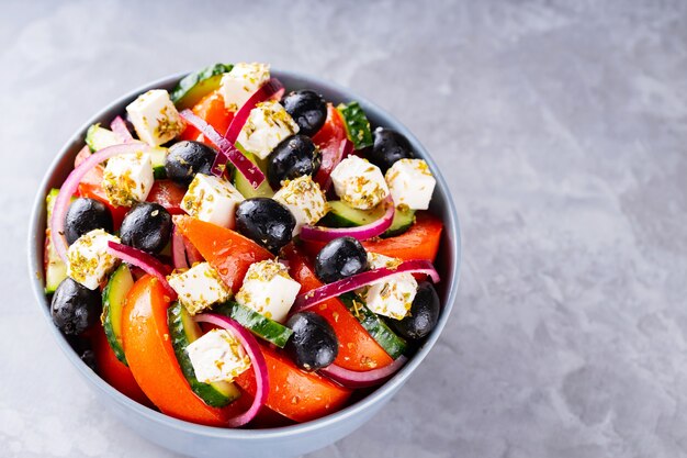 Griechischer Salat mit Feta und Oliven auf grauem Hintergrund. Gesunder mediterraner Salat. Platz kopieren. Ansicht von oben