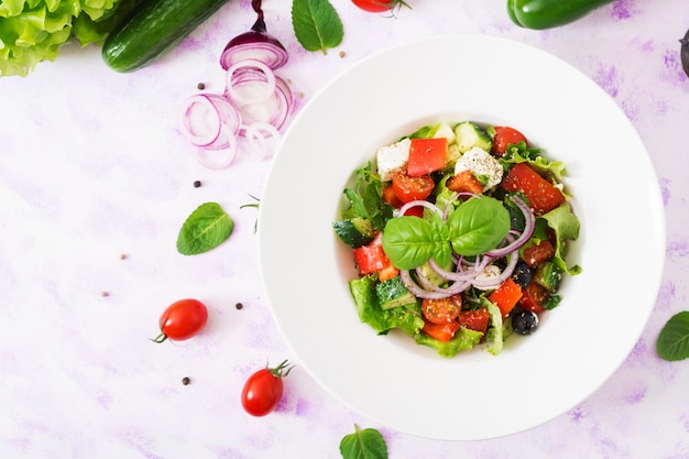 Griechischer Salat mit frischen Tomaten, Gurken, roten Zwiebeln, Basilikum, Salat, Feta-Käse, schwarzen Oliven und italienischen Kräutern. Draufsicht