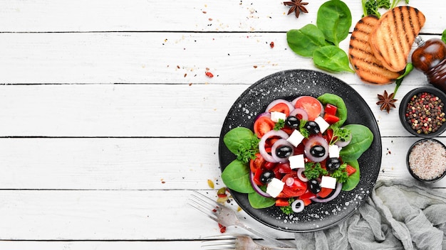 Griechischer Salat mit Tomaten Paprika Zwiebeln und Feta-Käse In einem schwarzen Teller auf einem hölzernen Hintergrund Ansicht von oben Freier Platz für Ihren Text Flach lag