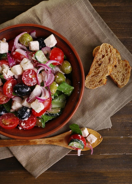 Griechischer Salat serviert in brauner Schüssel mit Brot auf Sackleinen auf Holzhintergrund