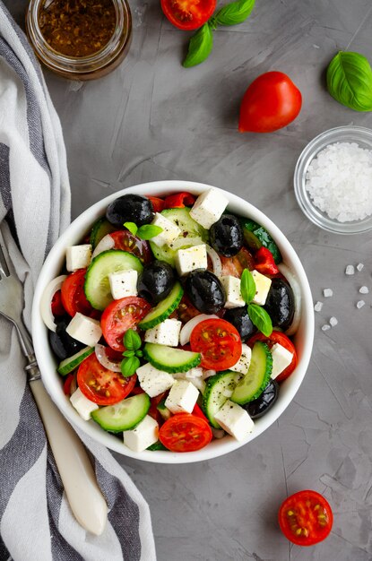 Griechischer Salat von frischem saftigem Gemüse, Feta-Käse, Kräutern und Oliven in einer weißen Schüssel auf einem dunklen Betonhintergrund. Gesundes Essen.