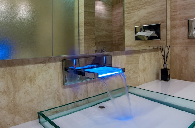 Grifo LED con caño en cascada sobre fregadero de vidrio en un elegante baño