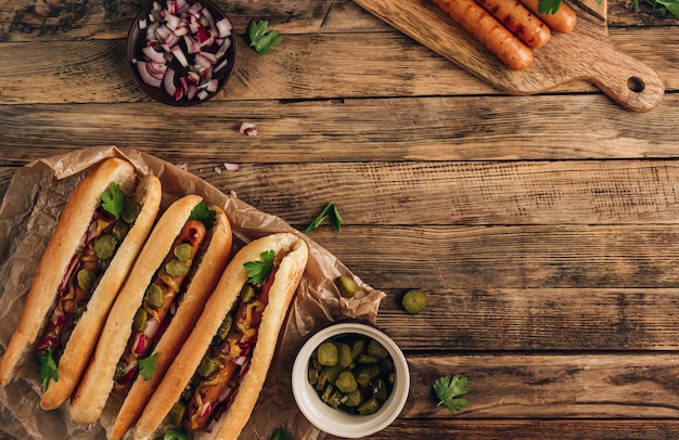 Grill gegrillter Hotdog mit eingelegter Gurke, roter Zwiebel und Senf auf rustikalem Holzhintergrund. Draufsicht mit Kopienraum