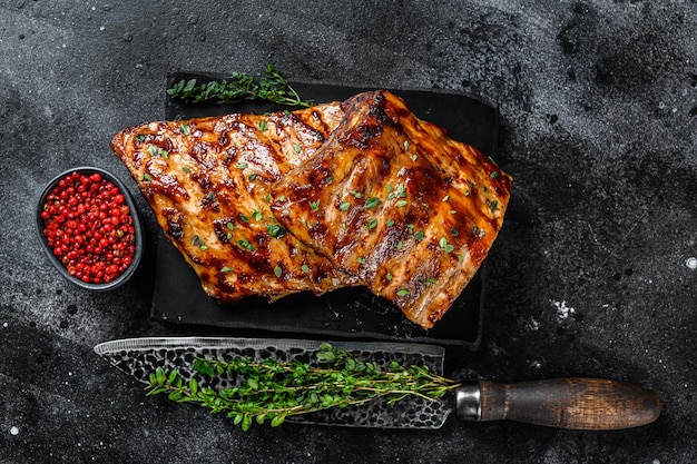 Grill-Schweinefleisch-Rack-Spare-Ribs auf einem Marmorbrett. Schwarzer Hintergrund. Ansicht von oben.