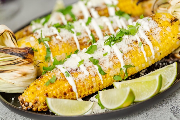 Grillen mexikanischer Straßenmais-Elote, garniert mit Gewürzen und frischem Koriander auf einer Servierplatte.