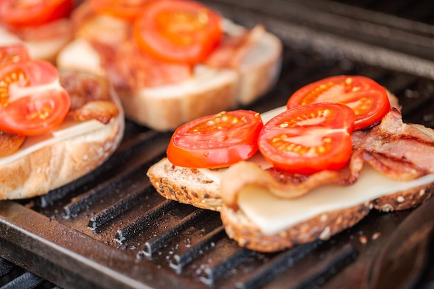 Grillen von gegrilltem Käsesandwich mit Speckstreifen und frischen Tomaten auf einem Gasgrill im Freien.