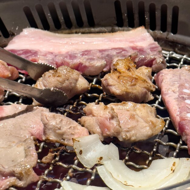 Grillen von Schweinebauchfleisch auf einem runden Grillnetz im Restaurant zum Essen