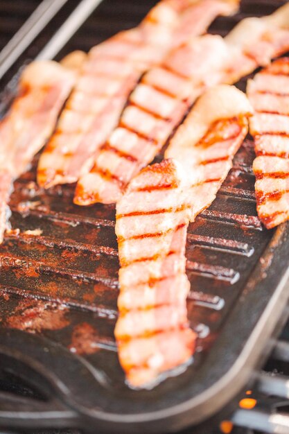 Grillen von Speckstreifen auf einer gusseisernen Grillplatte im Gasgrill im Freien.