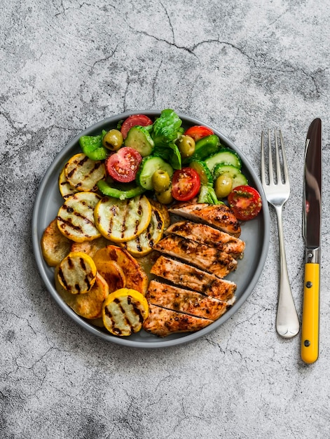 Grillplatte Hähnchenbrust gelbe Zucchini Grillkartoffeln und frischer Gemüsesalat mit Pesto-Sauce-Dressing auf grauem Hintergrund Draufsicht