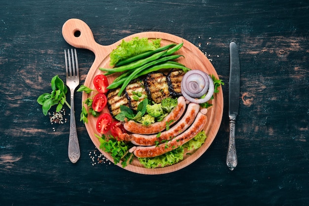 Grillwurst mit Auberginenbohnen und Tomaten auf dem Brett Gesundes Essen Auf einem schwarzen Holztisch Draufsicht Freier Platz für Text