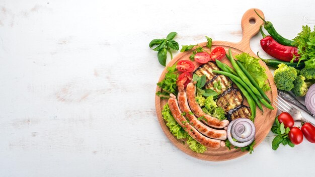 Grillwurst mit Auberginenbohnen und Tomaten auf dem Brett Gesundes Essen Auf einem weißen Holztisch Draufsicht Freier Platz für Text