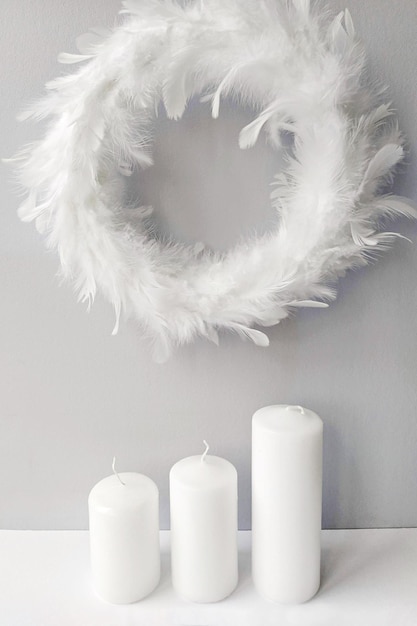 Grinalda branca felpuda feita de penas em uma parede com três velas grandes. decoração interior em estilo minimalista.