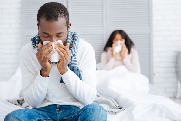 Gripe fatigosa. Bonita pareja joven que parece infeliz mientras se queda en casa y cura su terrible gripe