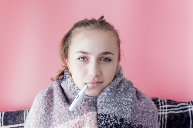 Gripe fría agarre. Mujer que tiene alta temperatura. Muchacha enferma con fiebre que controla el termómetro de mercurio en fondo rosado.