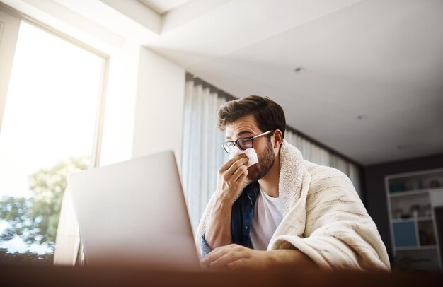 La gripe lo ha hecho trabajar desde casa hoy Foto de un joven empresario enfermizo sonándose la nariz con un pañuelo desechable mientras trabajaba desde casa