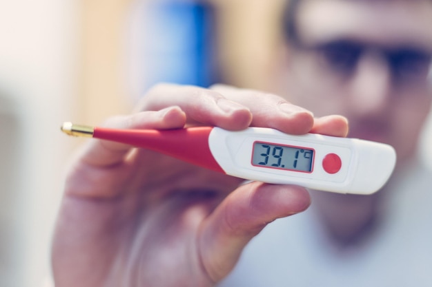 Grippe- und Corona-Konzept Der Mensch hält ein Fieberthermometer aus nächster Nähe in der Hand