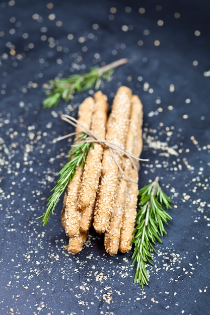 Grissini italiano o palitos de pan con sal y sésamo y romero en tablero negro.