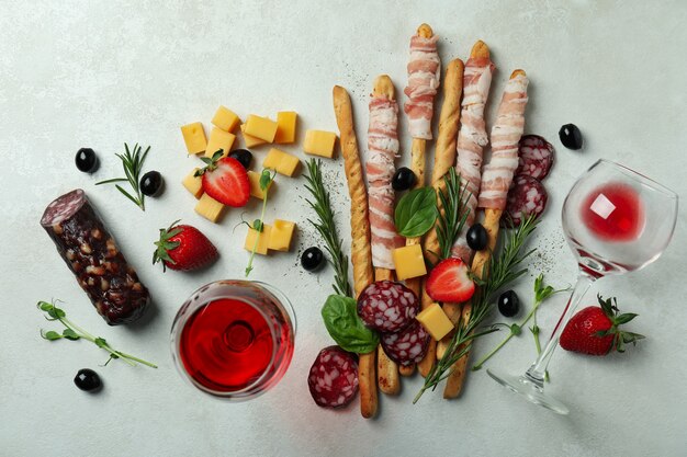 Grissini klebt mit Speck, Snacks und Wein auf weißem strukturiertem Hintergrund