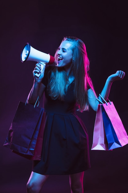 Gritando com sacolas de compras para vendas. retrato de jovem em luz de néon no fundo escuro. as emoções humanas, sexta-feira negra, cyber segunda-feira, compras, vendas, conceito de finanças.