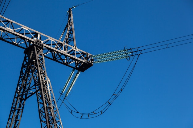 Grober Planmetallhochspannungspfosten mit vielen Drähten gegen einen blauen Himmel