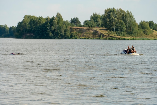 Grodno 22 de junho de 2021 Alguns caras estão nadando em um jet ski em um dia quente e ensolarado na superfície da água de um lago no fundo de uma floresta Um casal gay está descansando à beira-mar