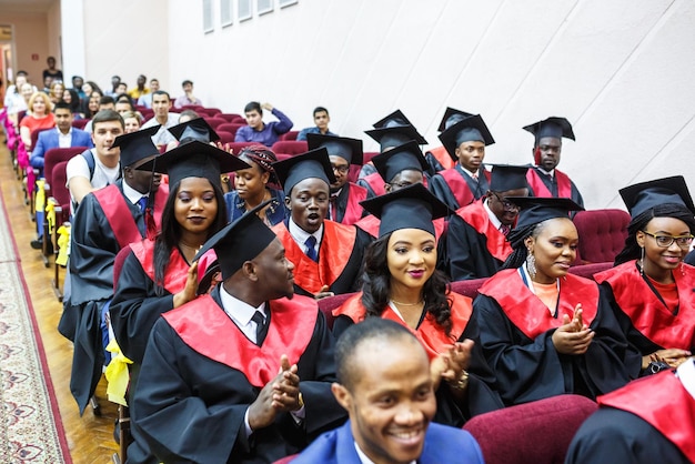 GRODNO BIELORRÚSSIA JUNHO DE 2018 Estudantes de medicina africanos estrangeiros em bonés quadrados de graduação acadêmica e capas de chuva pretas durante o início com diplomas fazem selfie