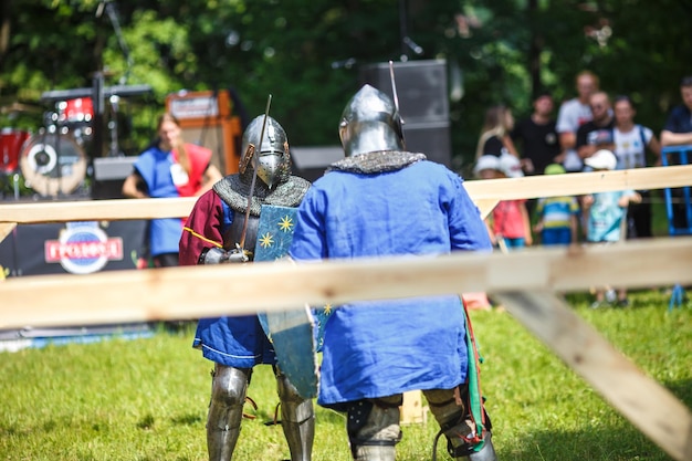 GRODNO BIELORRUSIA JUNIO DE 2019 Caballero de justas medievales lucha con cascos de armadura cota de malla con hachas y espadas en listas reconstrucción histórica de la antigua lucha