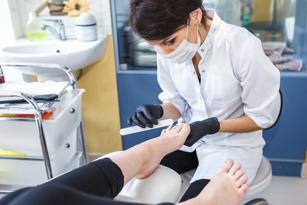 GRODNO BIELORRUSIA SEPTIEMBRE 2018 el maestro en guantes negros en el salón hace manicura pedicura al cliente