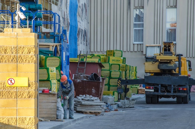 Grodno Bielorrússia 11 de outubro de 2018 Um homem de capacete e roupa de trabalho Aquecimento da fachada do edifício É um guindaste de torre Perto está um material de construção