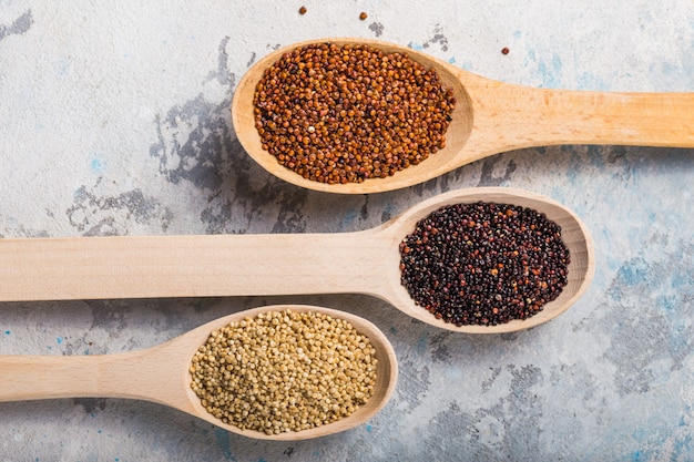Grões pretas, vermelhas e brancas do quinoa em uma colher de madeira no branco. comida saudável sem glúten. closeup de quinoa chenopodium