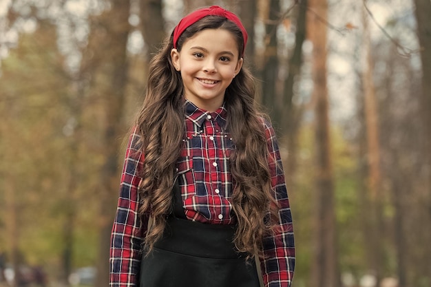 Größte Haar-Accessoire-Trends Entzückendes kleines Mädchen kariertes Hemd trägt rotes Stirnband Modetrend Accessoires Fancy Kind Natur Hintergrund Gepolstertes Stirnband Lächelndes Mädchen trägt geknotetes Stirnband