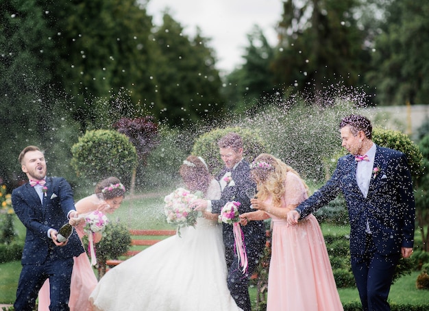 Groomsman öffnet eine Flasche Champagner vor Jungvermählten, die im Park stehen