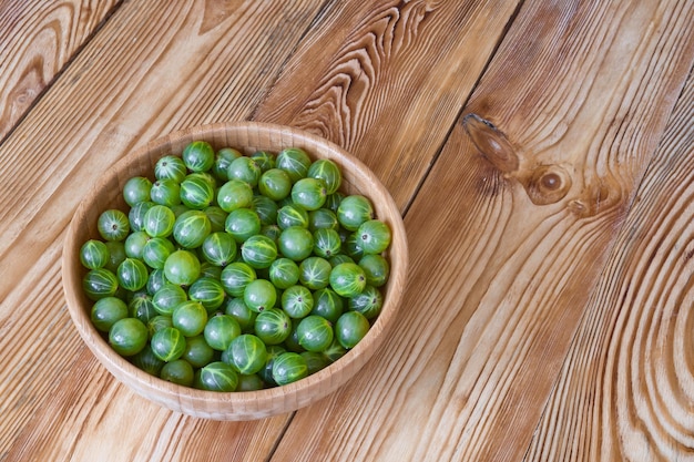 Groselhas verdes maduras em tigela na mesa de madeira