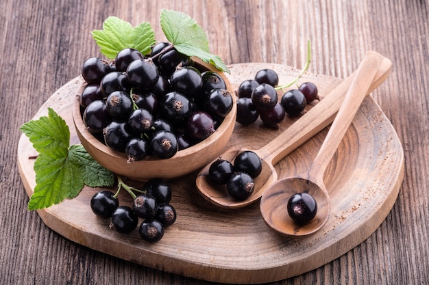 Grosella negra fresca madura en un tazón de madera con hojas originales y cucharas de remolque