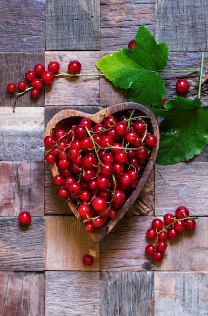 Grosellas rojas en un tazón en forma de corazón en una vista superior de fondo de madera vintage