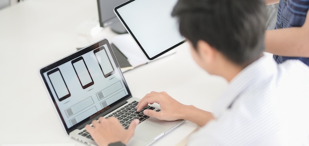 Großaufnahme des UI-Grafikdesigners planend auf seiner Smartphoneschablonenanwendung mit Laptop