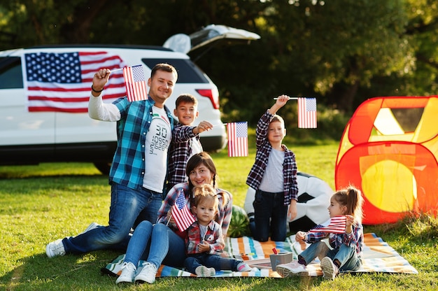 Große amerikanische Familie, die Zeit zusammen verbringt Mit USA-Flaggen gegen großes SUV-Auto im Freien. Amerika urlaub. Vier Kinder.