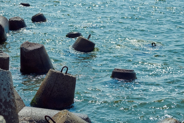 Große Betonwellenbrecher Tetrapoden in der Nähe von lebendigem Aquamarin Meer mit grellem Sonnenlicht auf der Wasseroberfläche, Nahaufnahme, Makro. Blöcke und Steine zum Schutz der Küste vor Sturm, schöne Meereslandschaft