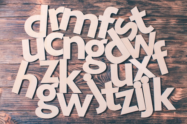 Große Buchstaben des Alphabets sind chaotisch auf Holzhintergrund verstreut. Konzept der Bildung