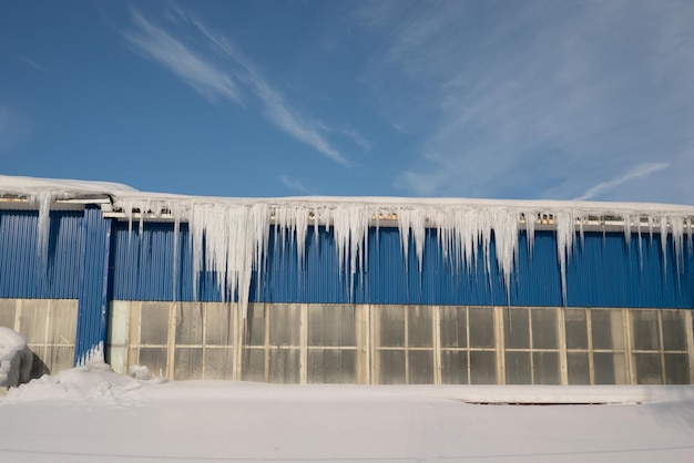 Große Eiszapfen auf dem Dach eines Stadthauses an einem verschneiten Wintertag unter Tauwetter Reinigung der Überdachung von Schnee und Eiszapfen