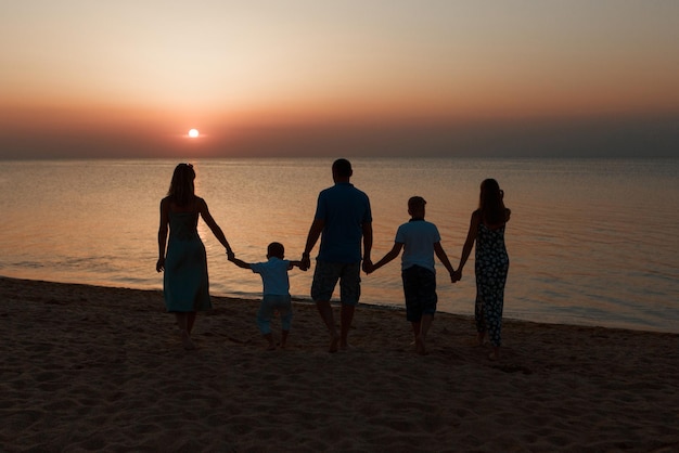 Große Familie am Strand. Silhouetten von Menschen gegen den Sonnenuntergang. 5 Personen, die Händchen halten