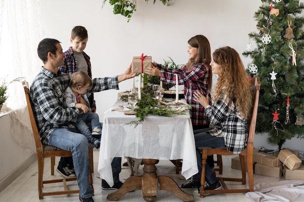 Große Familie hat ein Weihnachtsfrühstück am Tisch im Wohnzimmer Papa gibt einer kleinen Tochter für das neue Jahr eine Schachtel mit einem Geschenk Festlicher Tisch für Kinder und Eltern Frohes Weihnachtskonzept